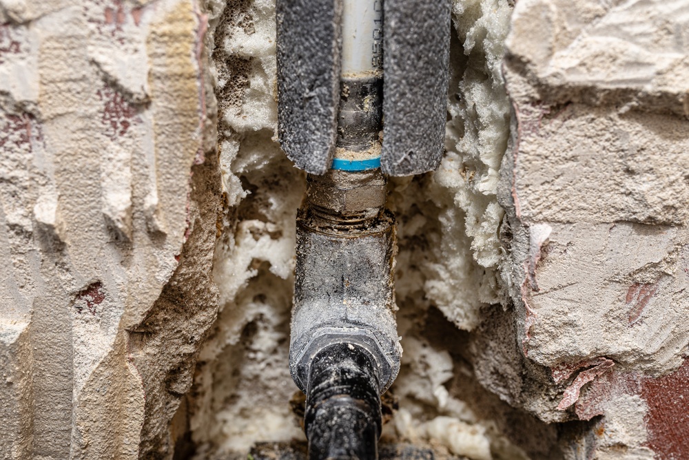 Plumber repairing a burst pipe while assessing repair costs inside a residential home